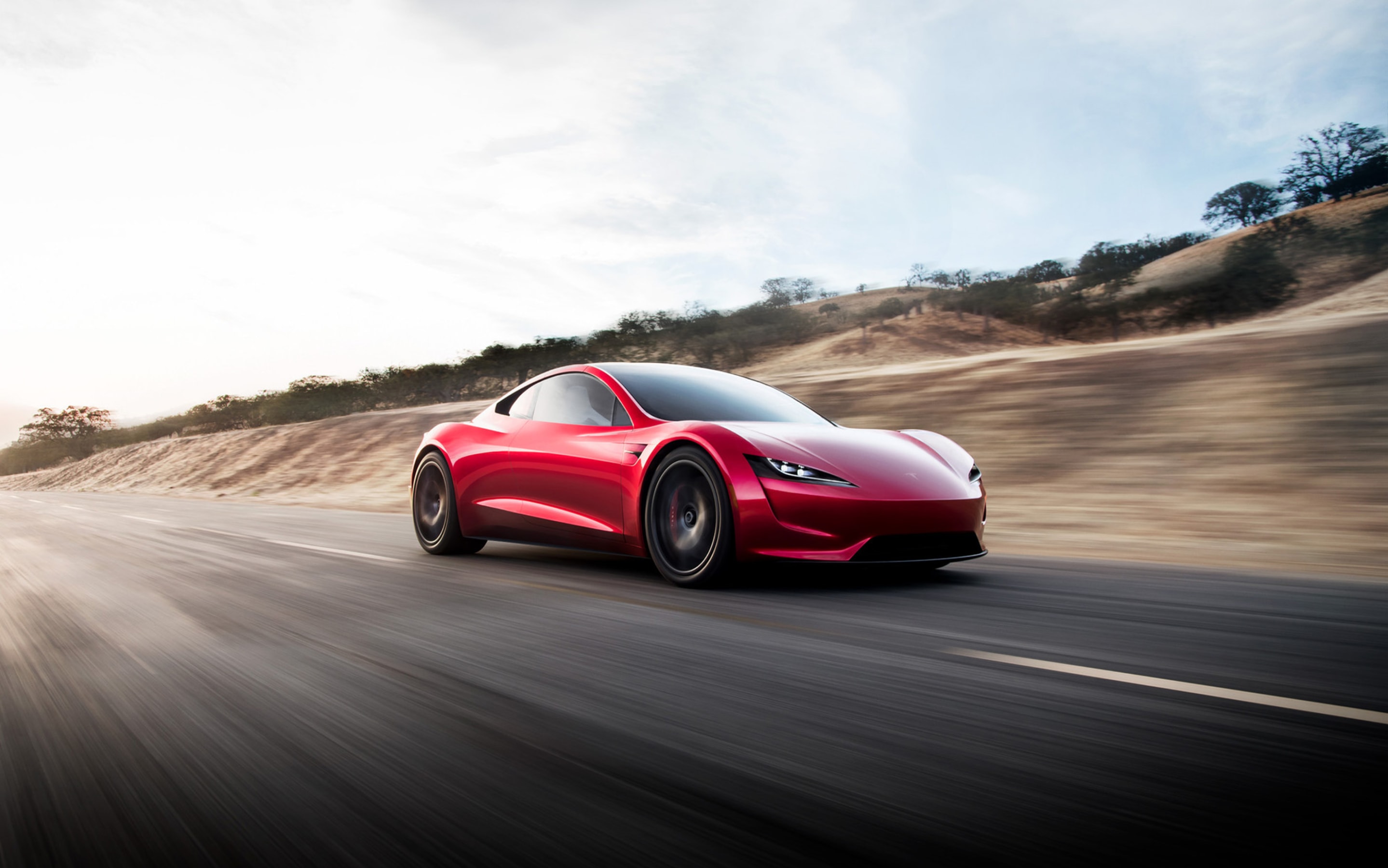 Tesla’s earlier red next-generation Roadster promotional image, showing the car on a paved road.